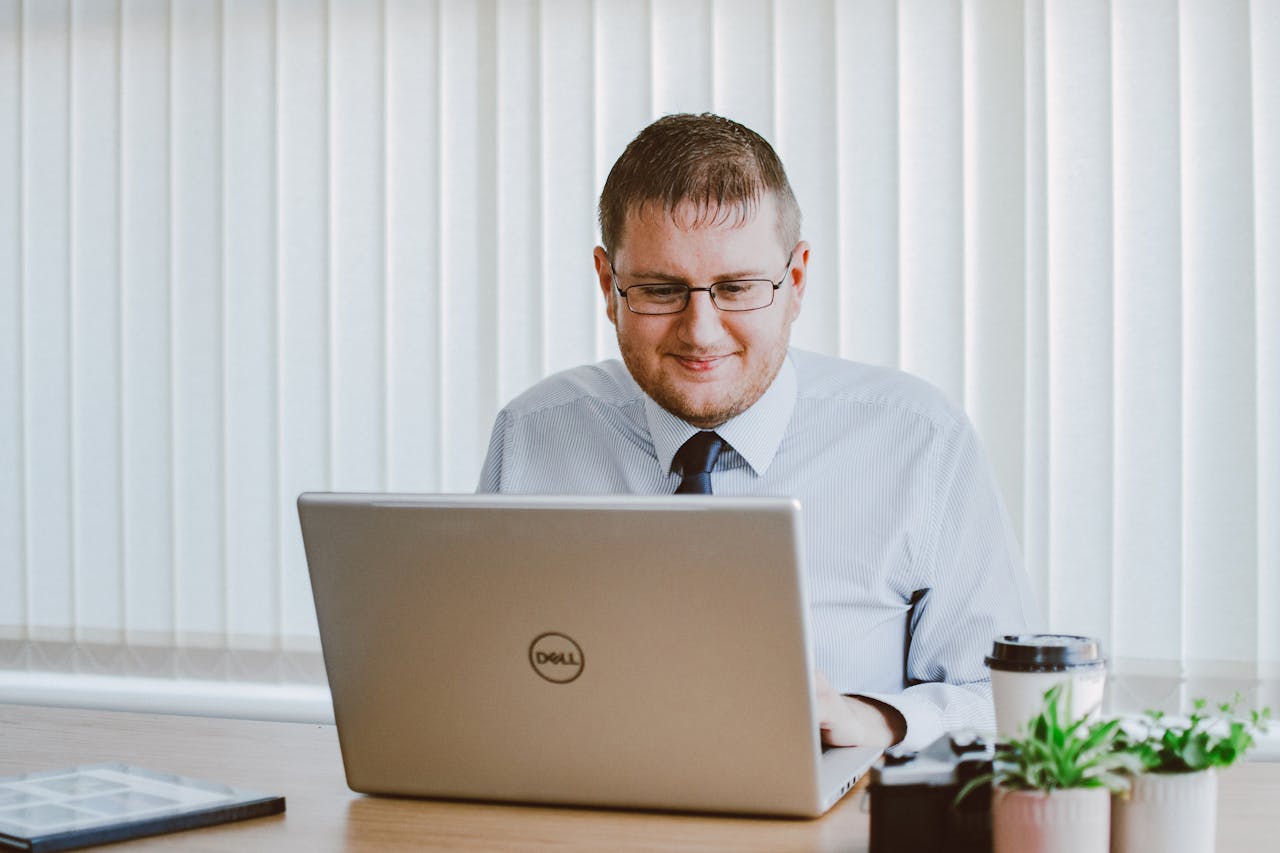 about-me-02 Business professional working on laptop at office desk with coffee and plants.